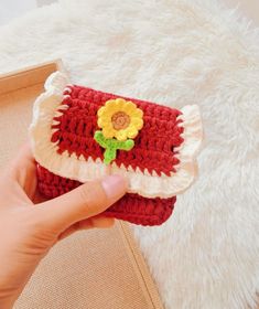 a hand holding a crocheted red and white purse with a yellow flower on it