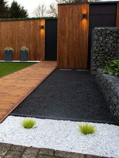 a wooden walkway leading to a garden with grass and rocks on the ground next to it