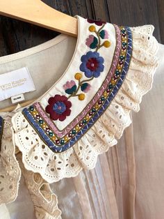 a white blouse with flowers and lace on the collar, hanging from a wooden hanger