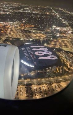 the view from an airplane window shows a stadium and city lights in the background at night