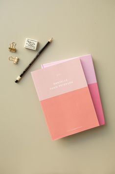 two pink notebooks sitting on top of a table next to a pair of pencils