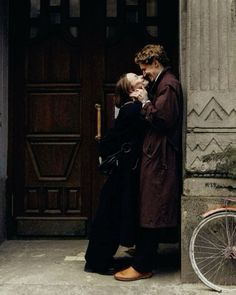 a man and woman standing in front of a door with a bicycle parked next to them