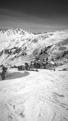 a black and white photo of snow covered hills with trees on the top one side