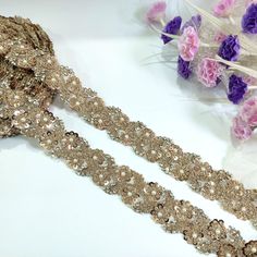 two pieces of beaded fabric next to some flowers and purple carnations on a white surface