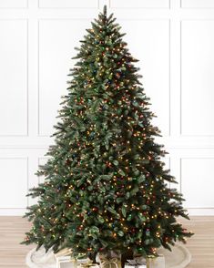 a small christmas tree with lights and presents on the floor in front of a white wall