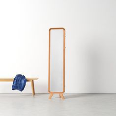 a mirror sitting next to a wooden bench on top of a cement floor in front of a white wall