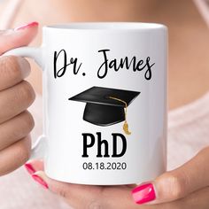 a woman holding a white coffee mug with a black graduation cap and tassel on it