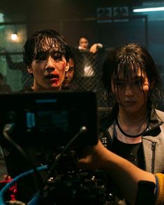 two people standing in front of a camera with blood on their face and one person behind the camera