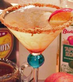 an apple cider cocktail garnished with sugar on the rim, sits in front of some liquor bottles