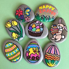 six painted rocks with easter eggs and flowers on them, sitting on a green surface