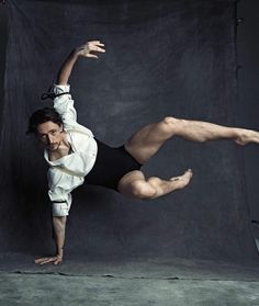 a man doing a handstand in front of a black backdrop with his legs spread out