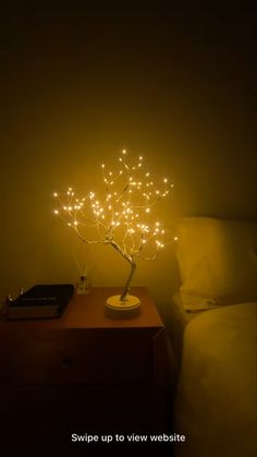 a small tree is lit up on a night stand next to a bed in the dark