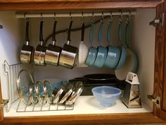 pots and pans are hanging on the wall in this kitchen cabinet with utensils