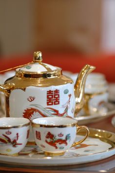 a tea set with gold trimmings and dragon designs on the china plate, sitting on a table