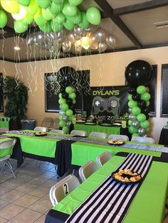 a party room with green and black tables, balloons and desserts on the table