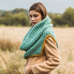 a woman standing in a field wearing a green knitted cowl with yellow trim