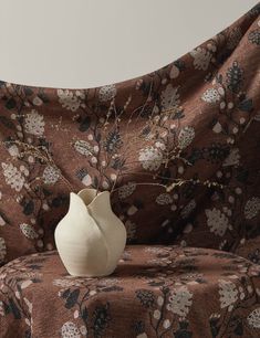 a white vase sitting on top of a brown floral print couch cover with branches sticking out of it