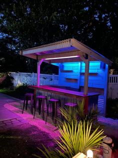 an outdoor bar lit up at night with purple lights and stools next to it