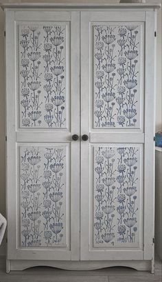 an old white cabinet with blue flowers painted on the doors and bottom panel is shown