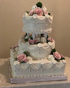 a three tiered wedding cake with pink roses on the top and bottom, sitting on a table