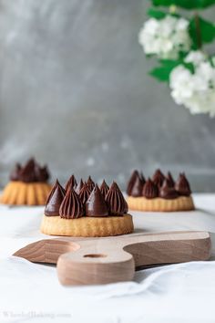 small desserts with chocolate frosting sitting on top of a cutting board next to flowers