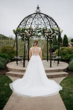 the back of a bride's dress as she stands on steps in front of an outdoor gazebo