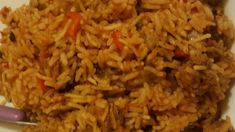 a white plate topped with rice and meat next to a purple handled utensil