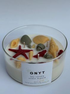 a glass bowl filled with different types of seashells and starfish on top of a white surface