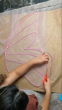 a woman is working on an art project with pink thread and plastic wings that are attached to canvases