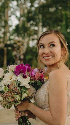 a woman in a wedding dress holding a bouquet of flowers and smiling at the camera