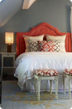 a bedroom with a red headboard and white bedding, two stools at the foot of the bed