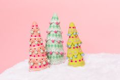 three small plastic christmas trees on top of a white furnishing covered surface against a pink background