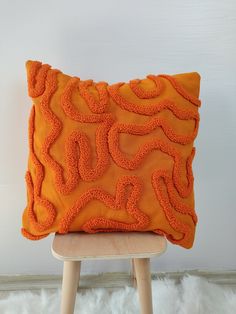 an orange decorative pillow sitting on top of a wooden stool in front of a white wall