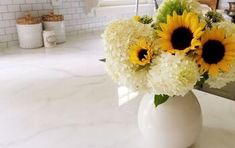 a vase filled with white and yellow flowers on top of a counter next to a sink