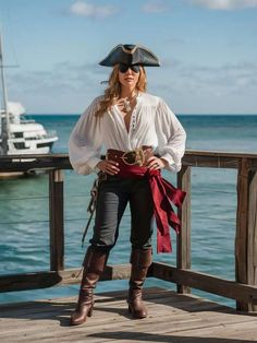 a woman in pirate costume standing on a dock near the ocean with her hands on her hips