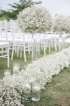 rows of white chairs with flowers in vases on the grass at an outdoor wedding ceremony