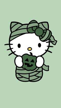 a hello kitty holding a pumpkin in her arms and wearing a green scarf on top of it