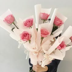 a woman holding a bunch of pink roses in her hands and wrapped in white paper