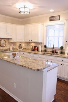 a large kitchen with white cabinets and granite counter tops on the island in front of the sink