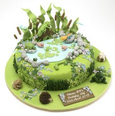 a birthday cake decorated with green and blue flowers, rocks, grass and plants on a plate