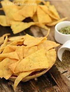 nacho chips in a basket on a wooden table next to two small bowls filled with seasoning