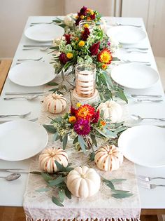 the table is set with white plates and pumpkins, flowers, and greenery