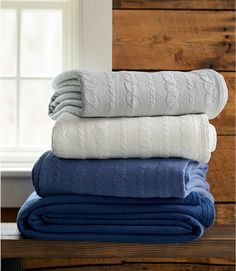 four folded blankets stacked on top of each other in front of a window with wood paneling