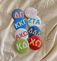 six buttons with letters and numbers on them sitting on a white cloth covered bed sheet