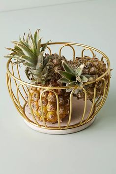 a pineapple sits in a wire basket on top of a white table with yellow trim