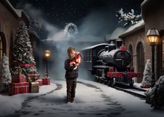 a young boy standing in front of a train with presents on the tracks next to it