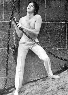 a shirtless man holding onto chains on the side of a building