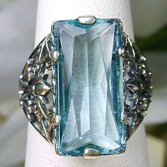 Sky Blue Aquamarine Ring Baguette Design#32 Introducing the Baguette D32, a stunning piece of wearable art that pays homage to the opulent Victorian era. Crafted with meticulous attention to detail, this exquisite filigree Antique reproduction in sterling silver is sure to captivate anyone with a love for vintage-inspired jewelry. At its center, lies a flawless 7ct sky blue gemstone, radiating a dazzling hue that catches the light with every movement. The baguette rectangle-cut gemstone measures Blue Gemstone Rings For Evening, Rectangular Sapphire Jewelry For Wedding, Elegant Engraved Blue Jewelry, Rectangular Aquamarine Blue Jewelry, Rectangular Blue Aquamarine Jewelry, Blue Rectangular Aquamarine Jewelry, Formal Blue Aquamarine Jewelry, Vintage Blue Aquamarine Jewelry, Formal Blue Jewelry With Intricate Design