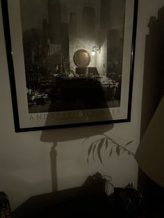 the shadow of a lamp on a wall in front of a framed photograph with a cityscape behind it