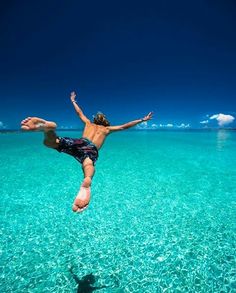 a man diving into the ocean with his feet in the air while wearing swim trunks